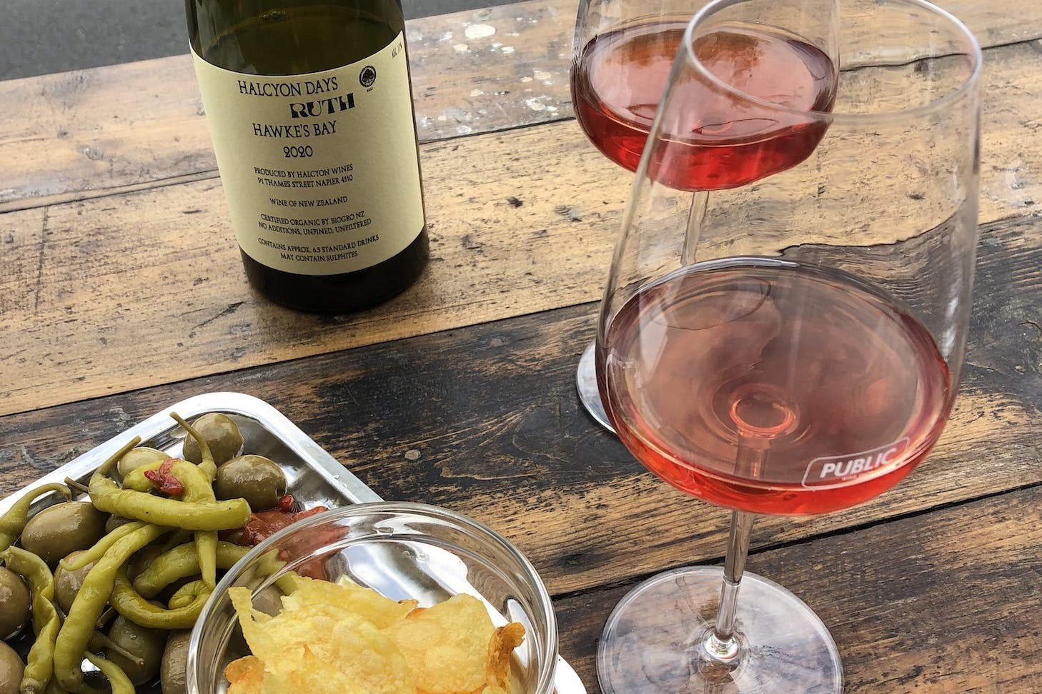Two glasses of light red natural wine on a bar table with a platter of snacks.